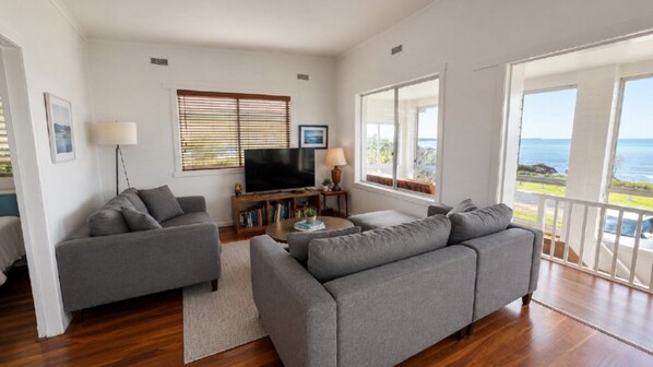 A living room with two grey sofas, a flat-screen TV, a coffee table, and a bookshelf.