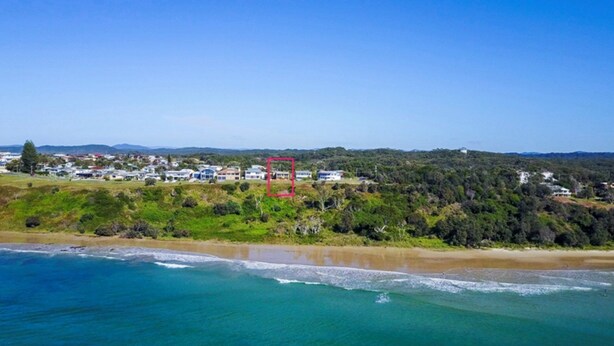 A coastal landscape with a beach, ocean, and a residential area with houses.