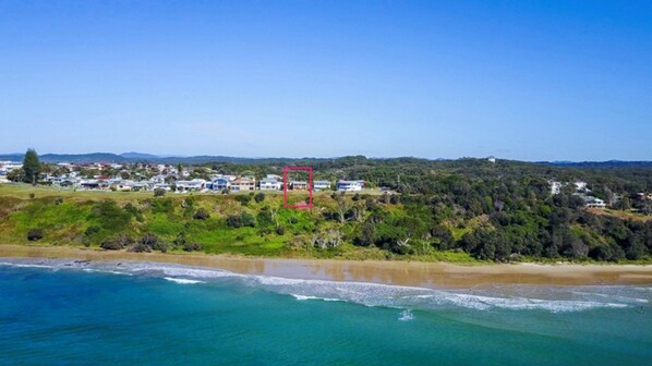 A coastal landscape with a beach, ocean, and a residential area with houses.
