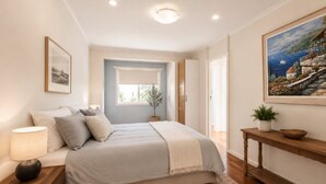 Quarto com cama, mesa de cabeceira, abajur e um quadro na parede.