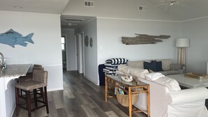A modern living room with a sofa, a coffee table, and a dining area with a bar. - Beachfront Home! Ready for the summer! (Galveston)