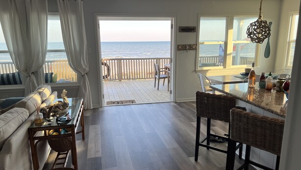 A spacious living area with a view of the ocean, a dining area with a kitchen counter, and a wooden deck. - Beachfront Home! Ready for the summer! (Galveston)