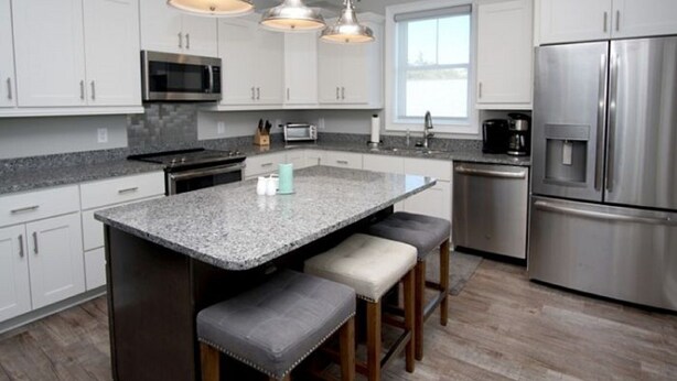 A modern kitchen with white cabinets, a granite countertop, a stainless steel refrigerator, and a built-in oven.