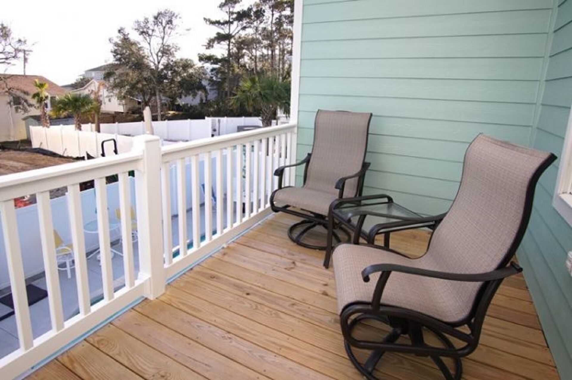 A wooden deck with two chairs and a white railing.