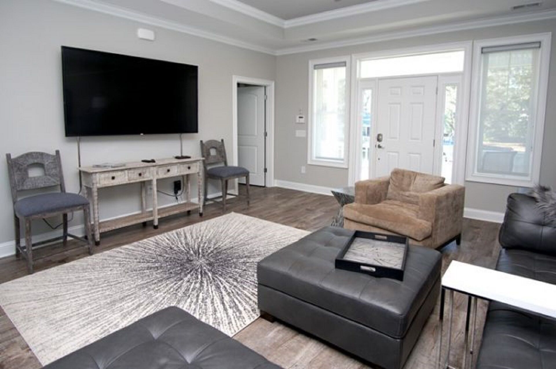 A modern living room with a flat-screen TV, a grey sofa, a brown armchair, and a coffee table.