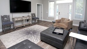 A modern living room with a flat-screen TV, a grey sofa, a brown armchair, and a coffee table.