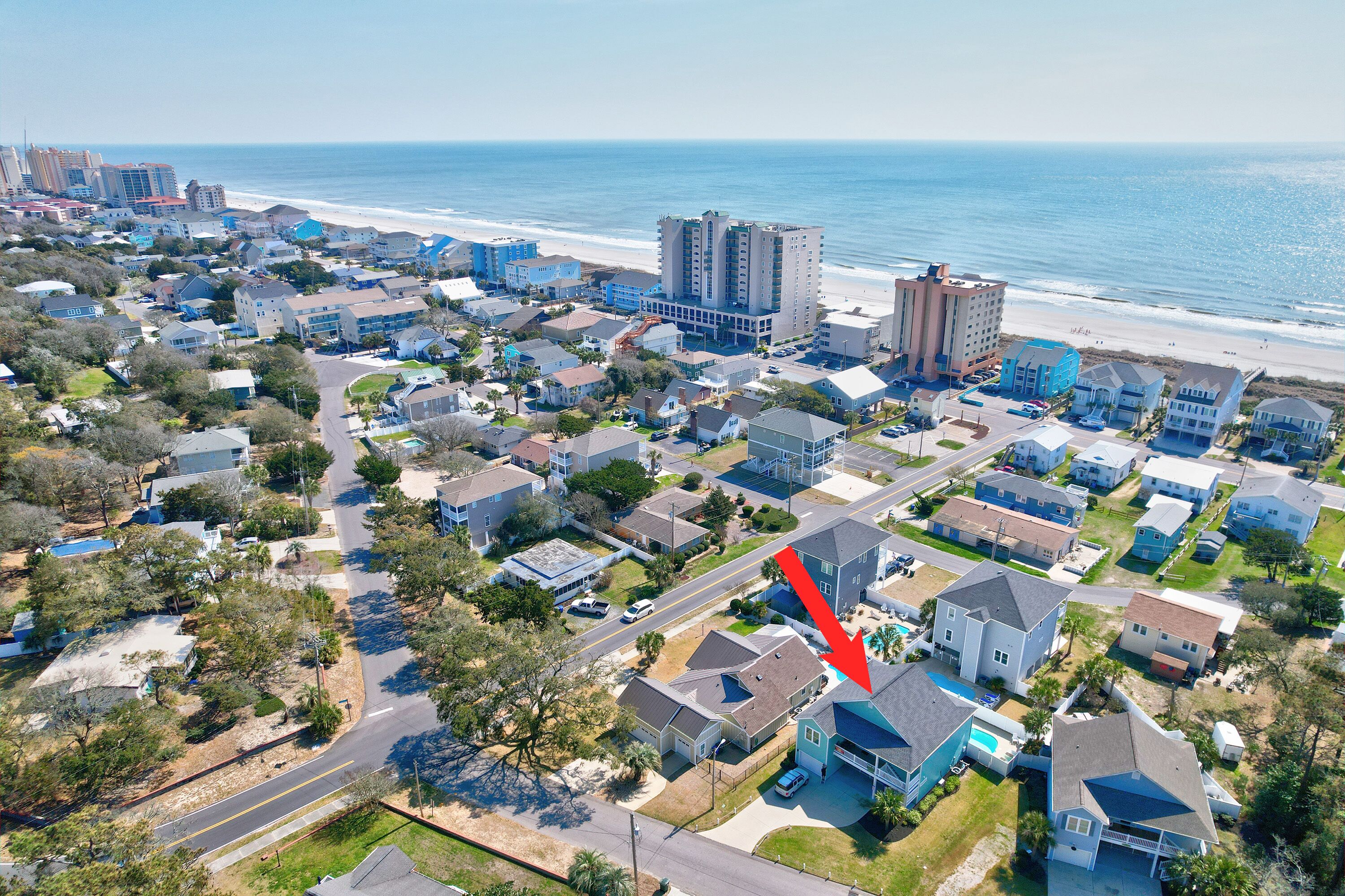 An aerial view of a coastal residential area with houses, a beach, and high-rise buildings.