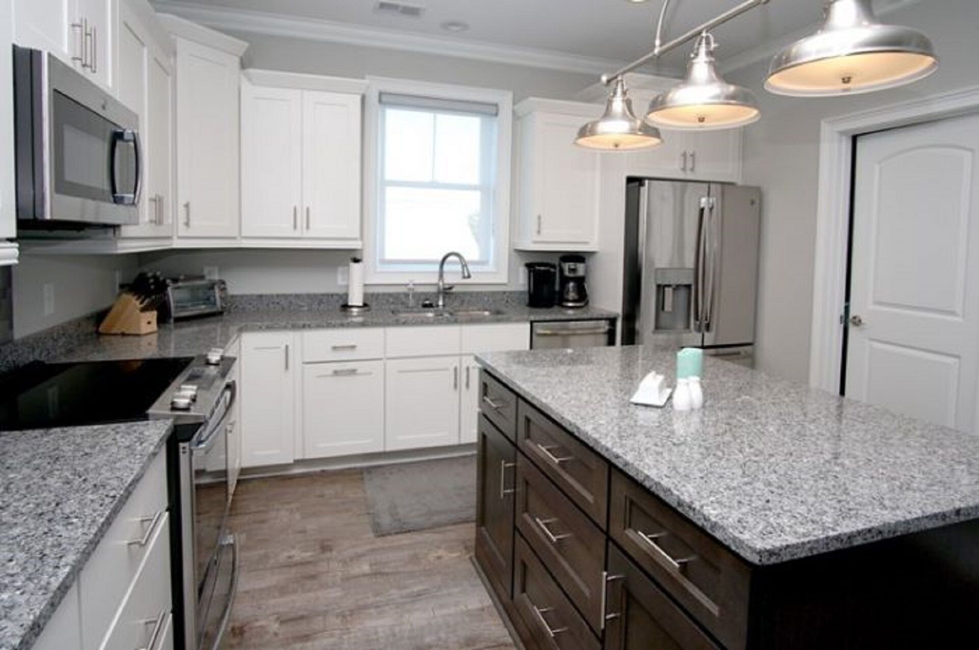 A modern kitchen with white cabinets, granite countertops, stainless steel appliances, and pendant lighting.
