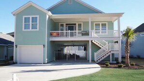 A two-story house with a front garage, a balcony on the upper floor, and a palm tree in the front yard.