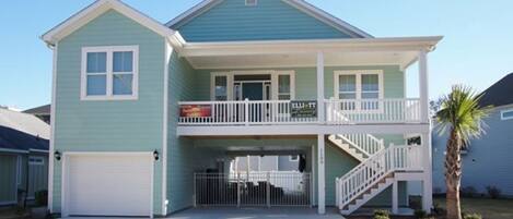 A two-story house with a front garage, a balcony on the upper floor, and a palm tree in the front yard.
