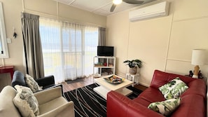A living room with a sofa, armchair, coffee table, and a television on a stand.