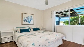 A bedroom with a bed, a nightstand, a wall-mounted artwork, and a window with a view of greenery.