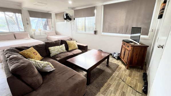 A modern living room with a sofa set, a coffee table, a TV on a wooden cabinet, and a window with a view.