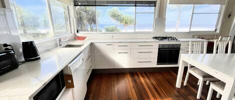 Una cocina moderna con armarios blancos, piso de madera y ventanas amplias con vistas a un paisaje natural.