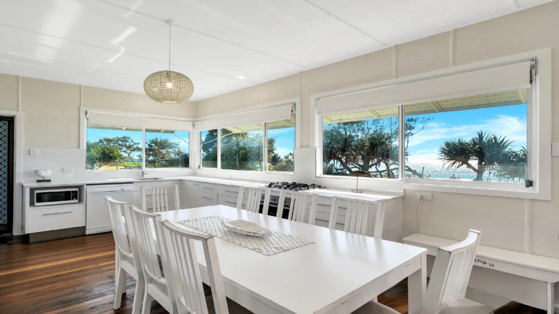 A modern kitchen with white cabinetry, a dining table, and large windows offering a view of the outdoors.