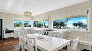 A modern kitchen with white cabinetry, a dining table, and large windows offering a view of the outdoors.