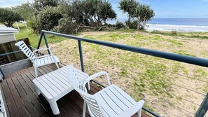A wooden deck with white plastic chairs, overlooking a beach with a view of the ocean.