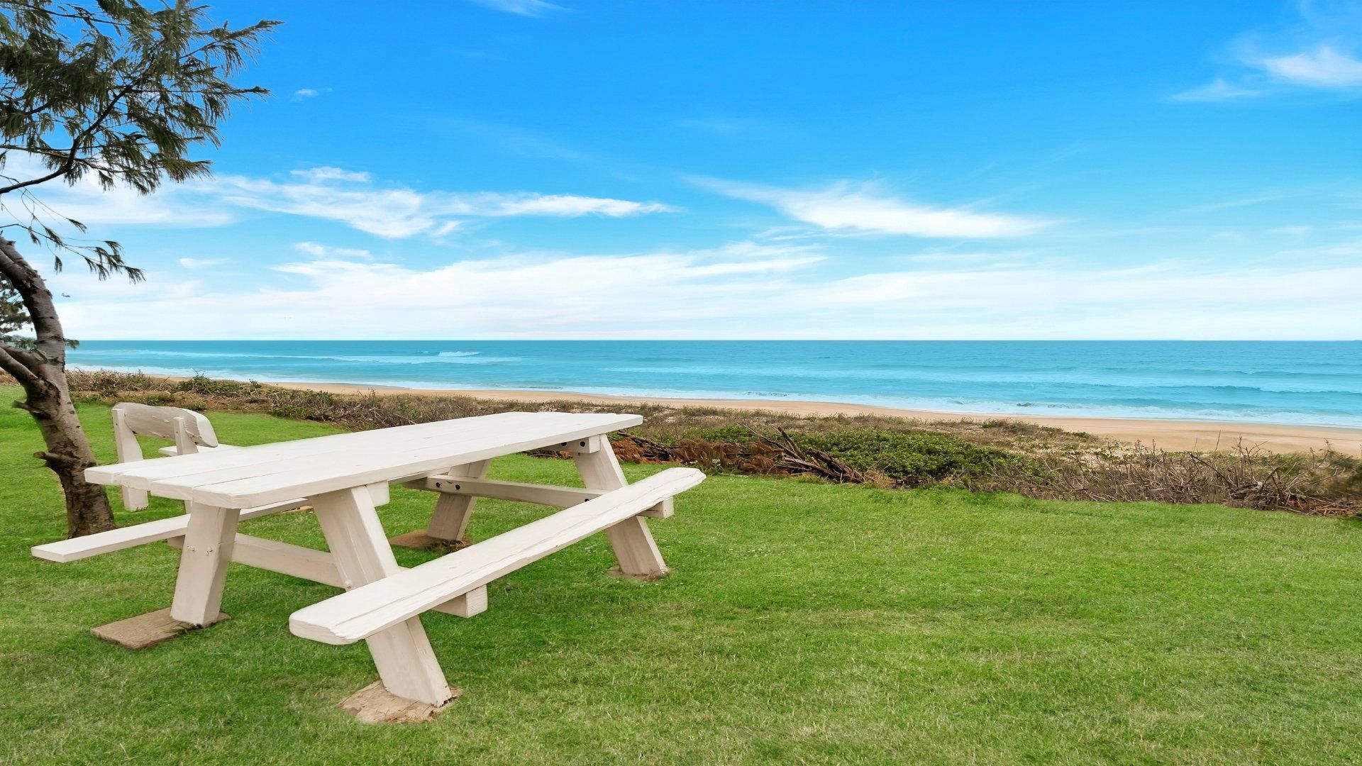 A picnic table with benches on a grassy area overlooking a beach.