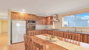 A kitchen with wooden cabinets, a stainless steel refrigerator, a microwave, an oven, a gas stove, and a large island with chairs.