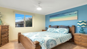 A bedroom with a bed, a dresser, a nightstand, a lamp, a window, and a painting on the wall.