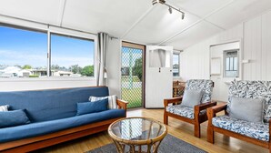 A modern living room with a blue sofa, patterned armchairs, and a glass coffee table. - The Purple Cottage - Burrum Heads - Walk To Beach -2BR -... (BURRUM HEADS)