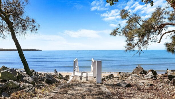 A beach with a wooden bench and a concrete structure, surrounded by rocks and trees. - The Purple Cottage - Burrum Heads - Walk To Beach -2BR -... (BURRUM HEADS)