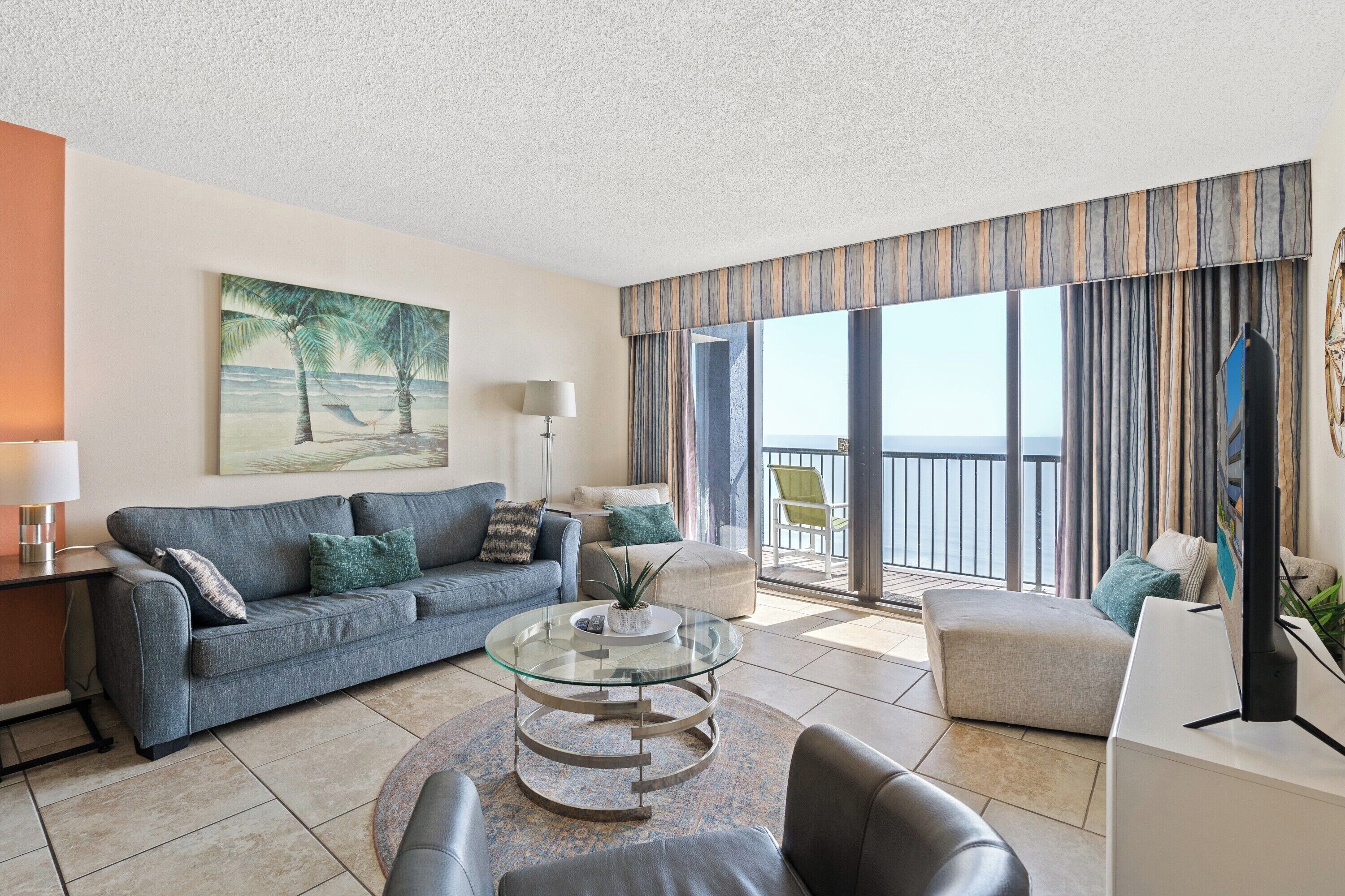 A modern living room with a sofa, a glass coffee table, a side table, and a painting of a beach scene.
