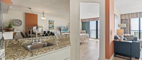A modern kitchen with granite countertops, a sink, and a dining area with a sofa and a table.