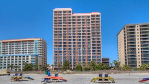 A high-rise hotel with multiple floors, a beach in the foreground, and palm trees.