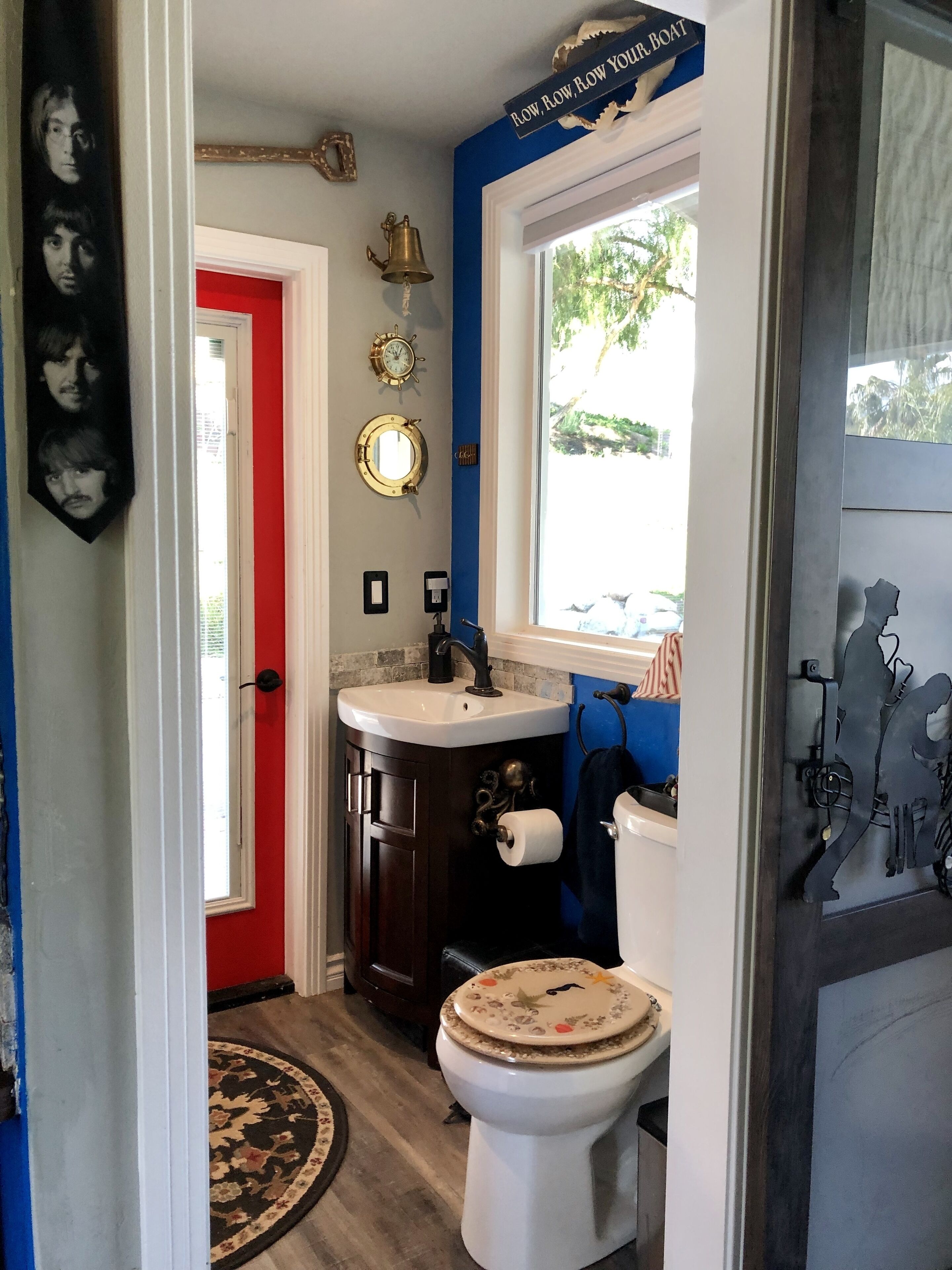 Une salle de bain avec une porte rouge, un lavabo, des toilettes et une fenêtre donnant sur l’extérieur.