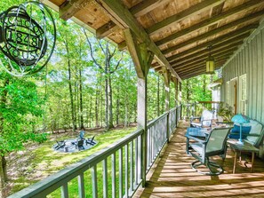 A covered porch with a wooden deck, outdoor seating, and a view of a forested area. - Unlock a Forgotten Past at The Schoolhouse Cottage · Dog-Friendly (Dahlonega)