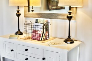 A white dresser with two black lamps, a wire basket with papers, and a framed picture on the top.