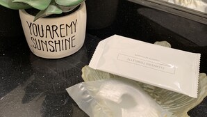 Ein im Blumentopf stehendes Sukkulentenpflänzchen mit einem Schildchen mit der Aufschrift 'YOUAREMY SUNSHINE' und einer Packung 'CLEANSING TOWEL' auf einer spiegelnden Oberfläche.