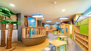 Zona de juegos infantiles con una estructura tipo barco, mesas, sillas y estanterías de colores.