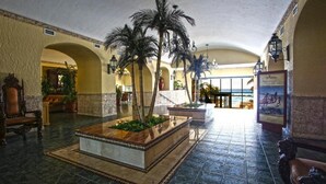 Un hall con una jardinera central, palmeras y vista al mar.