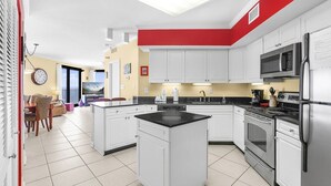 A modern kitchen with white cabinets, a black countertop island, stainless steel appliances, and a red accent wall. - Windward Pointe 1401 : Beachfront Corner Condo w/ Wrap-Around Gulf Views (Orange Beach)