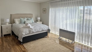 Une chambre à coucher comprenant un lit, des tables de chevet, un ventilateur de plafond, un radiateur et des rideaux légers.