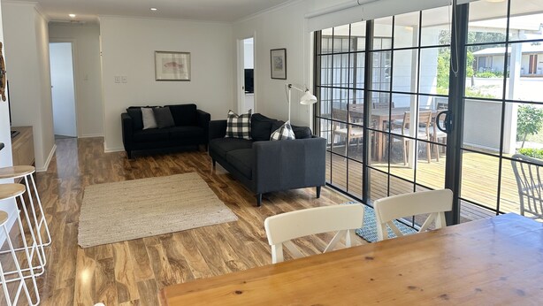 Un salon spacieux avec un canapé gris foncé, une table à manger en bois et une grande fenêtre donnant sur l’extérieur.