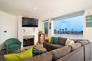 Ein Wohnzimmer mit Fernseher, Kamin, Sofa und Blick auf Strand und Parkplatz.