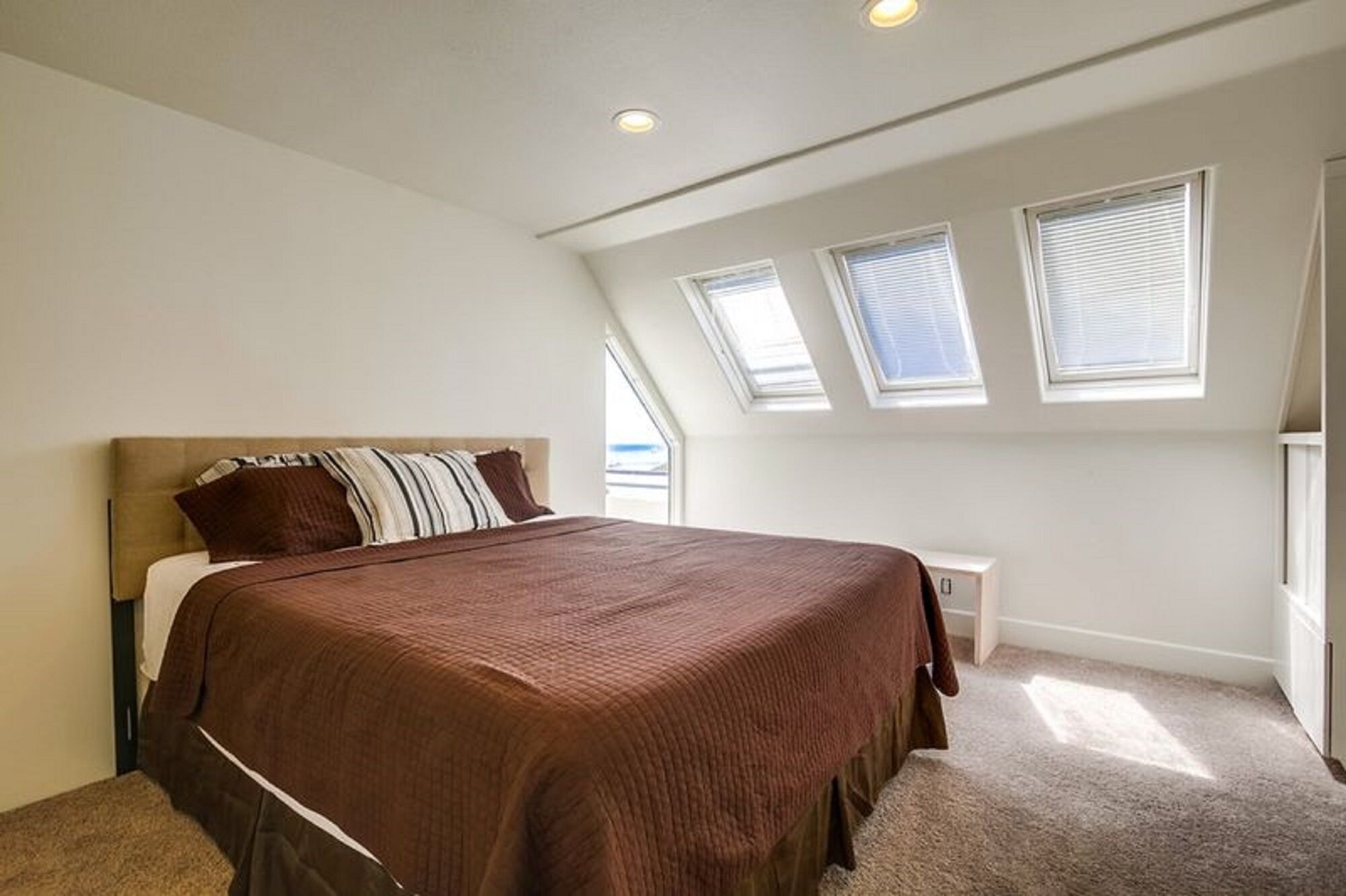 A bedroom with a large bed, a nightstand, and skylights.