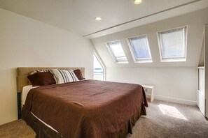 A bedroom with a large bed, a nightstand, and skylights.