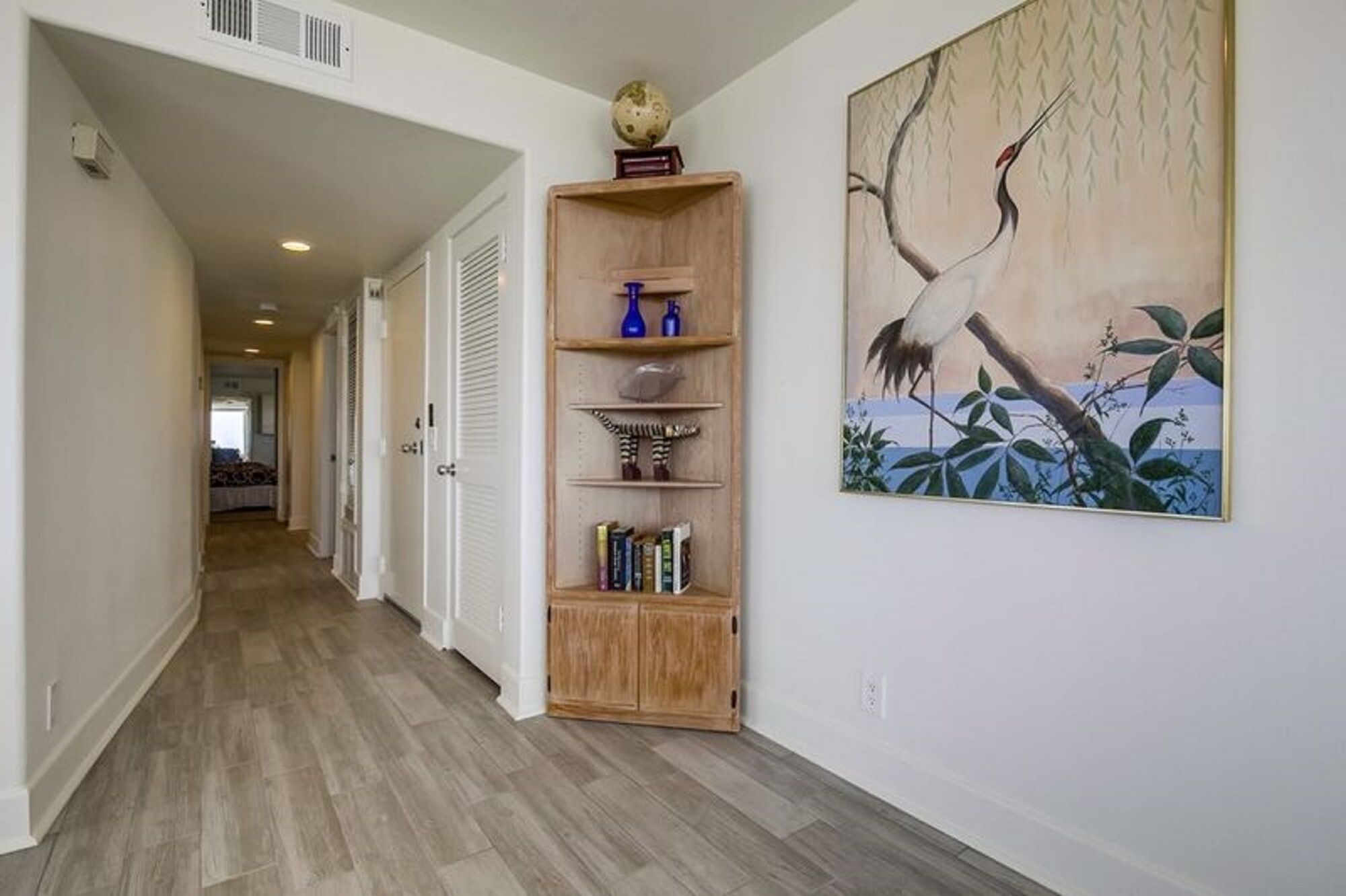 A hallway with a wooden bookshelf, a painting, and a view into another room.