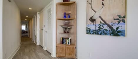 A hallway with a wooden bookshelf, a painting, and a view into another room.
