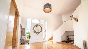 A spacious room with wooden flooring, a large mirror, a staircase, and a ceiling light fixture. - Rathescar Grove (Dunleer)