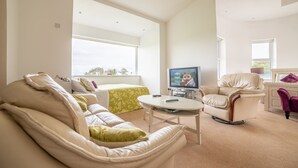 A modern living room with a sofa, a green accent chair, a television, and a window with a view. - Rathescar Grove (Dunleer)