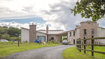 A modern building with a stone facade, a circular window, and a gravel driveway leading to a wooden fence.