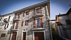 A multi-story stone building with balconies, wooden shutters, and a visible ground floor entrance. - VICTORY HOUSE 4 FRONT LAKE AP3 GARDEN & SPA (Colmegna)