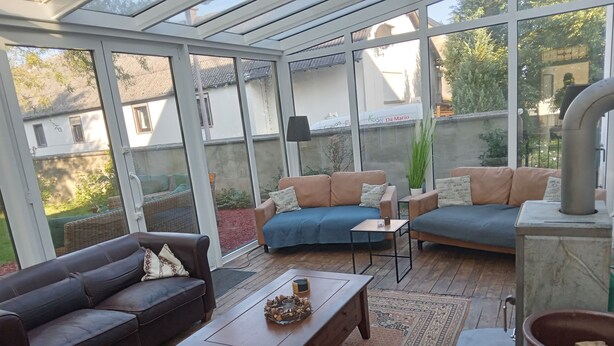 Una habitación iluminada por el sol con techo de cristal, amoblada con un sofá de cuero marrón, un sofá azul y una mesa de centro de madera.