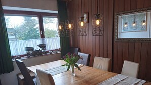 Un comedor con mesa de madera, sillas, un jarrón de flores y lámparas colgantes.