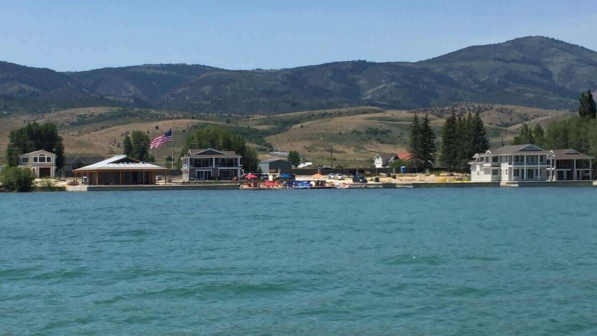 A lakeside property with multiple buildings, including a large house with a covered porch and a smaller house with a flag.